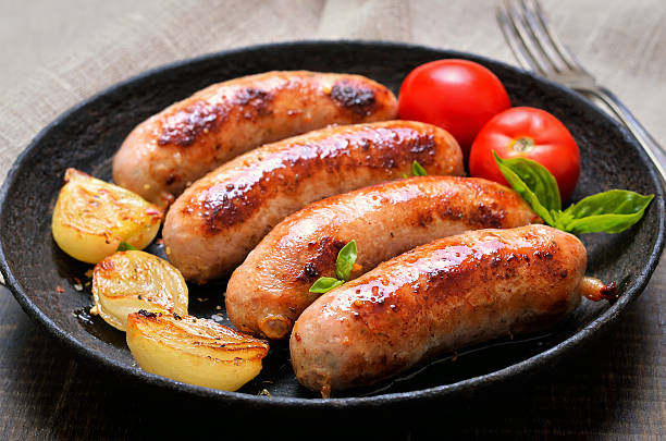 A plate of grilled sausages served with roasted onions and fresh tomatoes