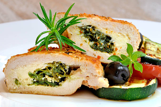 Close-up of a sliced stuffed chicken breast filled with spinach and cheese, garnished with herbs, served with vegetables.