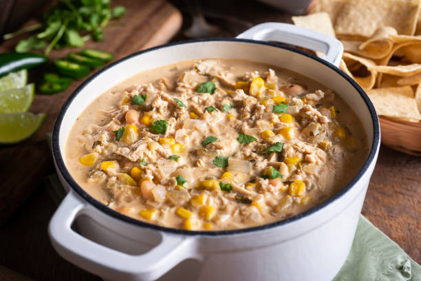 A creamy chicken corn chowder in a white pot garnished with cilantro, served with tortilla chips on the side.