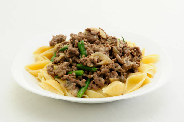 A delicious plate of pasta topped with sautéed beef and green beans served in a white dish.