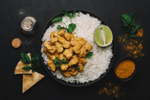 A plate of chicken curry served with white rice, garnished with fresh cilantro and lime slices, alongside pita bread and spices.