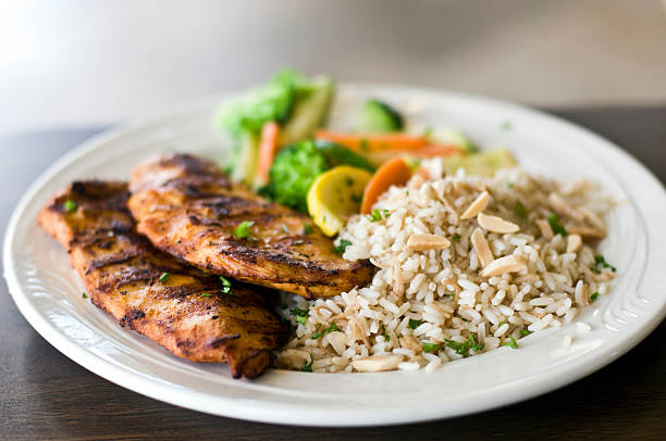 A plate of grilled chicken fillets served with rice and mixed vegetables.