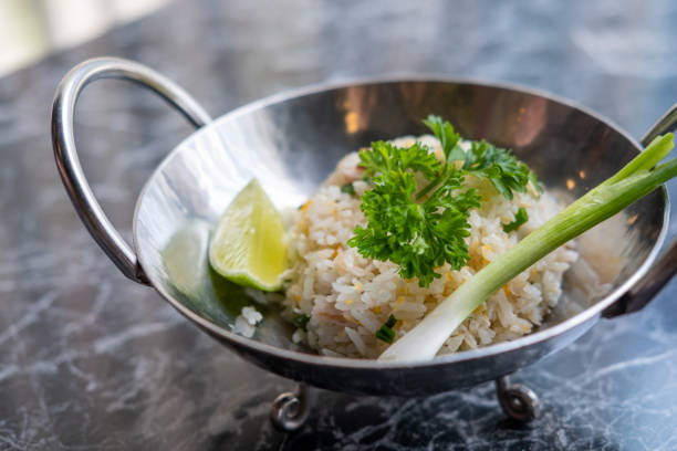 A bowl of fried rice garnished with fresh parsley and a lime wedge, served on a marble table.