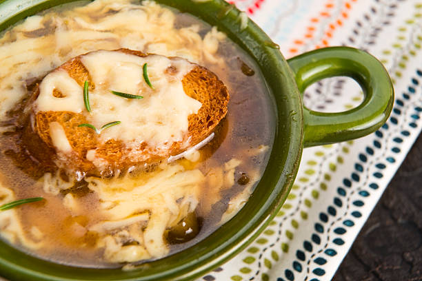 A bowl of cheese soup with a slice of toasted bread topped with melted cheese and garnished with herbs.