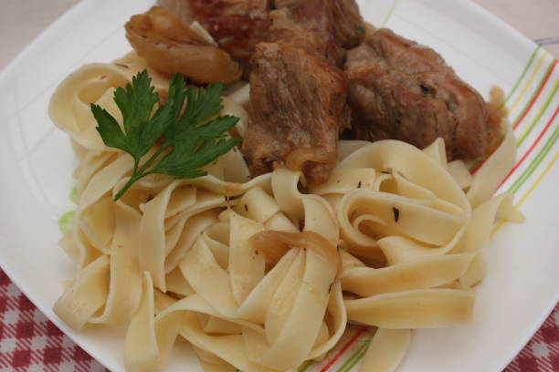 A plate of fettuccine pasta served with tender meat and garnished with a sprig of parsley.