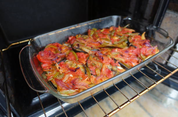 A glass dish containing baked vegetables, including tomatoes and green peppers, in an oven.