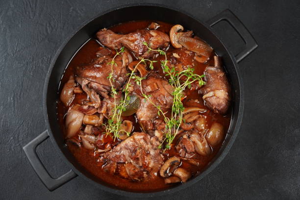 A pot of cooked chicken with mushrooms, onions, and herbs in a rich sauce.