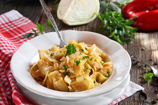 A bowl of pasta with parsley garnish on a rustic wooden table, accompanied by fresh vegetables.