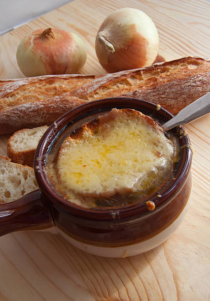 A bowl of French onion soup topped with melted cheese, surrounded by fresh onions and a baguette.