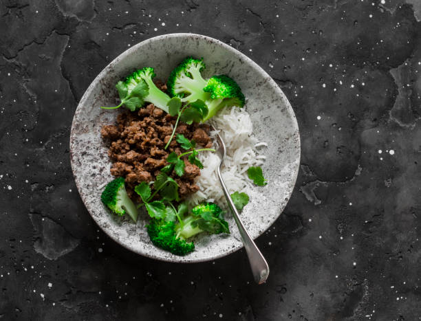 A bowl of ground meat, broccoli, and rice on a dark textured surface.