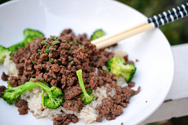 A bowl of rice topped with seasoned ground beef and broccoli, with chopsticks resting on the side.