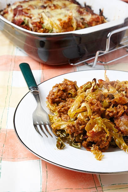 A plate of cooked cabbage with ground meat and a fork, with a baking dish of lasagna in the background.