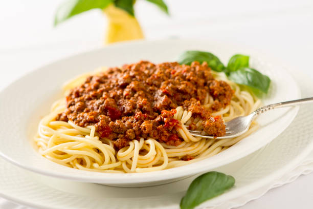 A plate of spaghetti topped with a rich meat sauce and garnished with fresh basil leaves.