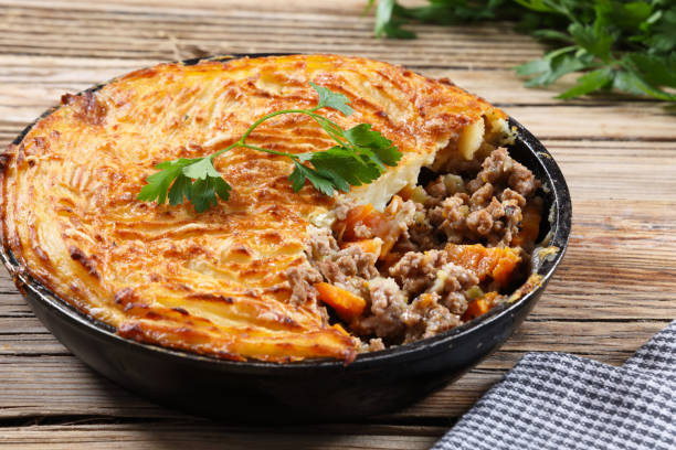 A delicious shepherd's pie in a black baking dish with a golden crust and a portion taken out, revealing a filling of minced meat and vegetables.