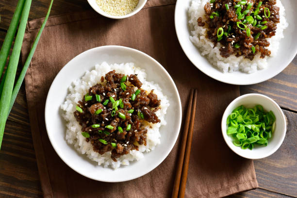 Two bowls of rice topped with savory meat and green onions, garnished with sesame seeds, on a wooden table.