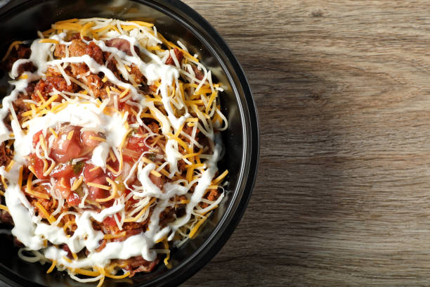 A delicious bowl of layered ingredients including beans, ground meat, shredded cheese, and sour cream placed on a wooden surface.