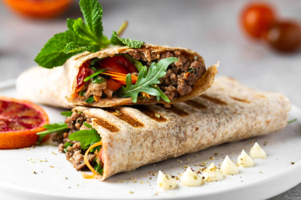 A delicious wrap filled with ground beef, fresh vegetables, and herbs on a white plate.