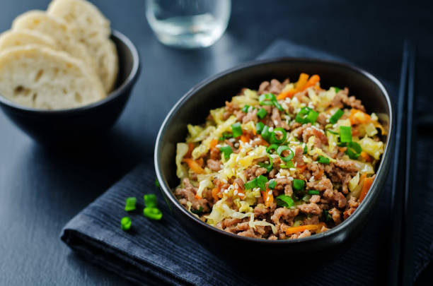 A bowl of stir-fried meat and vegetables topped with green onions, alongside a plate of flatbread.