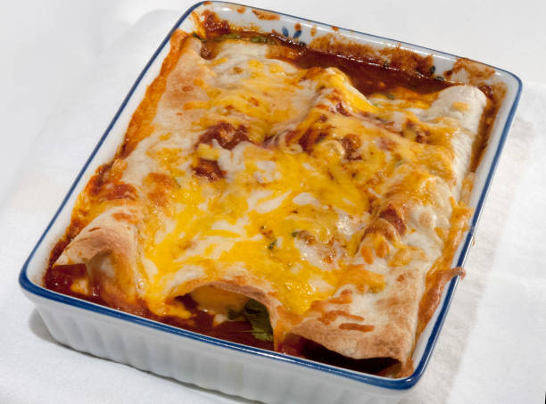 Baked enchiladas topped with melted cheese in a white ceramic dish