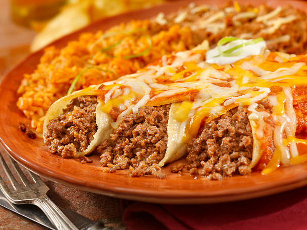 A plate of enchiladas filled with ground beef, topped with melted cheese, accompanied by yellow rice.