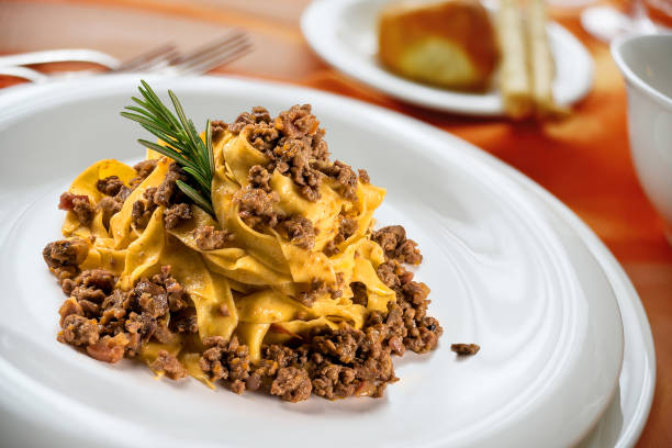 Plate of tagliatelle pasta topped with ground beef and garnished with a sprig of rosemary.