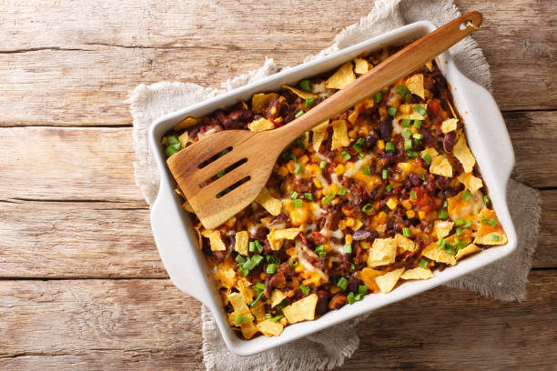 A delicious baked nacho casserole with cheese, beans, and tortilla chips, served in a white dish with a wooden spoon.