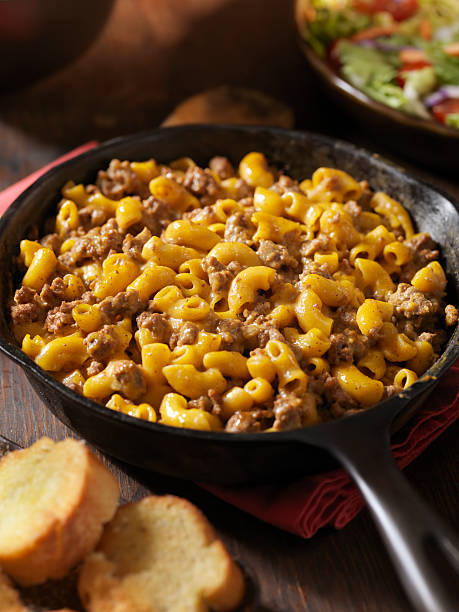 A skillet filled with creamy macaroni and cheese topped with ground beef, alongside slices of bread.