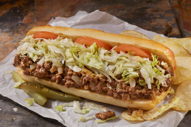 A delicious sandwich filled with ground beef, shredded lettuce, and sliced tomatoes, accompanied by chips and pickles.