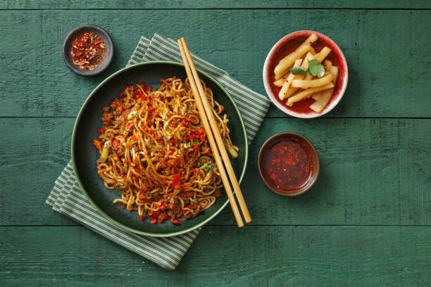 A delicious plate of stir-fried noodles topped with red chili flakes, served with chopsticks and accompanied by side dishes.