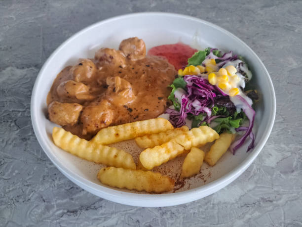 A bowl of food containing meatballs in sauce, crinkle-cut fries, and a side salad with corn and purple cabbage.