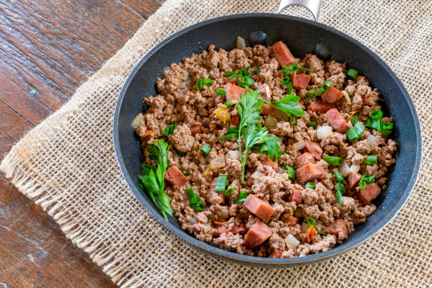 A black skillet filled with cooked ground beef and diced sausage, garnished with chopped green onions and parsley.