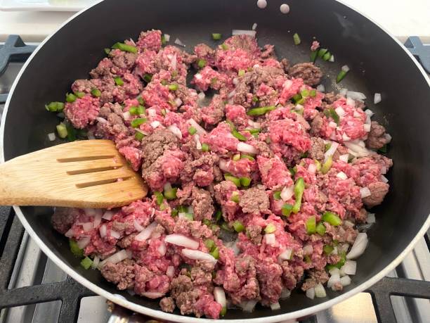 Browned ground beef mixed with chopped green bell peppers and onions in a skillet.