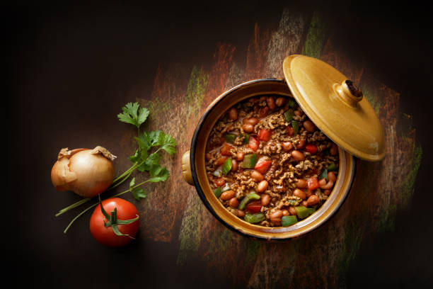 A pot of savory chili with beans and vegetables, surrounded by fresh ingredients including tomatoes, onions, and cilantro.