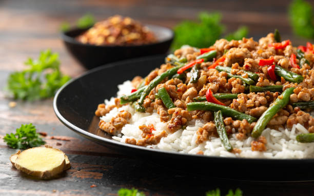 A plate of rice topped with minced meat and green beans, garnished with red chili slices, with a side of crushed red pepper.