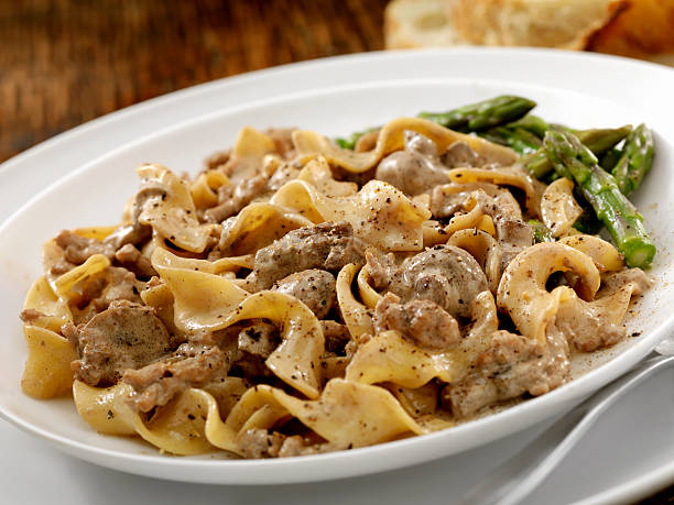 A plate of noodles with creamy meat sauce and asparagus on the side