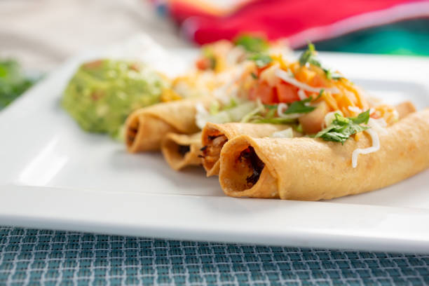 A plate of three delicious golden taquitos topped with fresh ingredients, served with guacamole on the side.