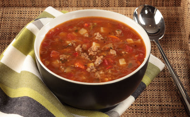 A bowl of hearty meat soup served on a striped napkin.