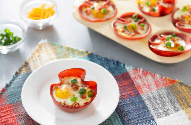 A plate with a baked egg in a red bell pepper half, garnished with green onions, with more similar dishes in the background.