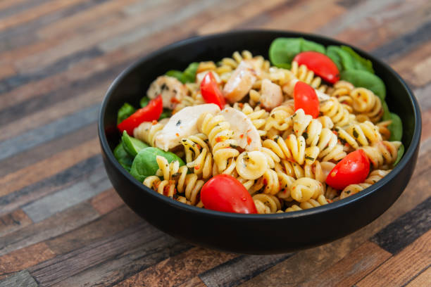 A bowl of pasta salad with rotini pasta, grilled chicken, cherry tomatoes, and spinach.