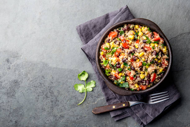 Bowl of quinoa salad with black beans, corn, tomatoes, and cilantro on a dark stone surface