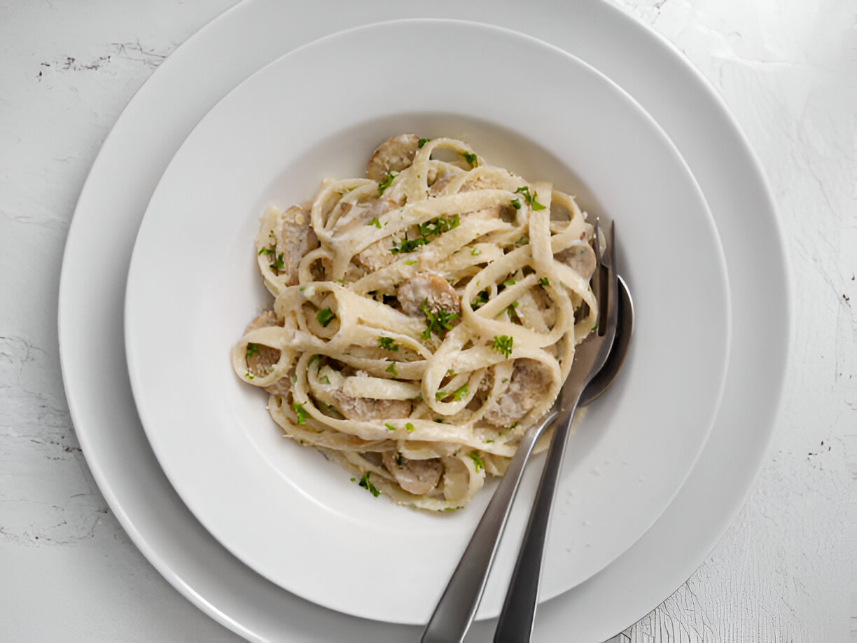 A bowl of fettuccine pasta with creamy sauce and herbs, served on a white plate.