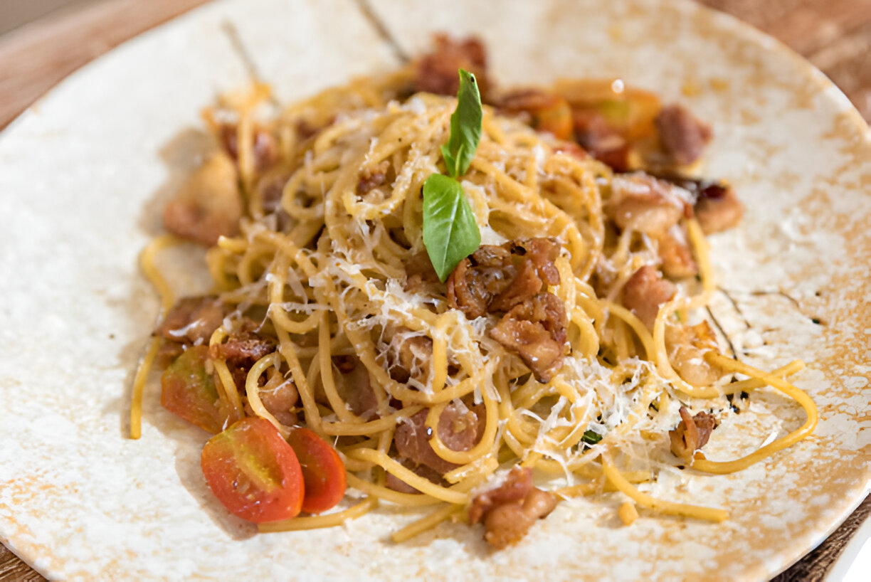 A plate of spaghetti topped with herbs, cheese, and diced bacon