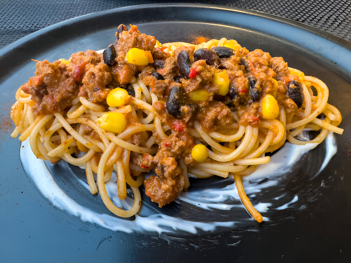 A plate of spaghetti topped with a mixture of ground meat, black beans, corn, and tomatoes.