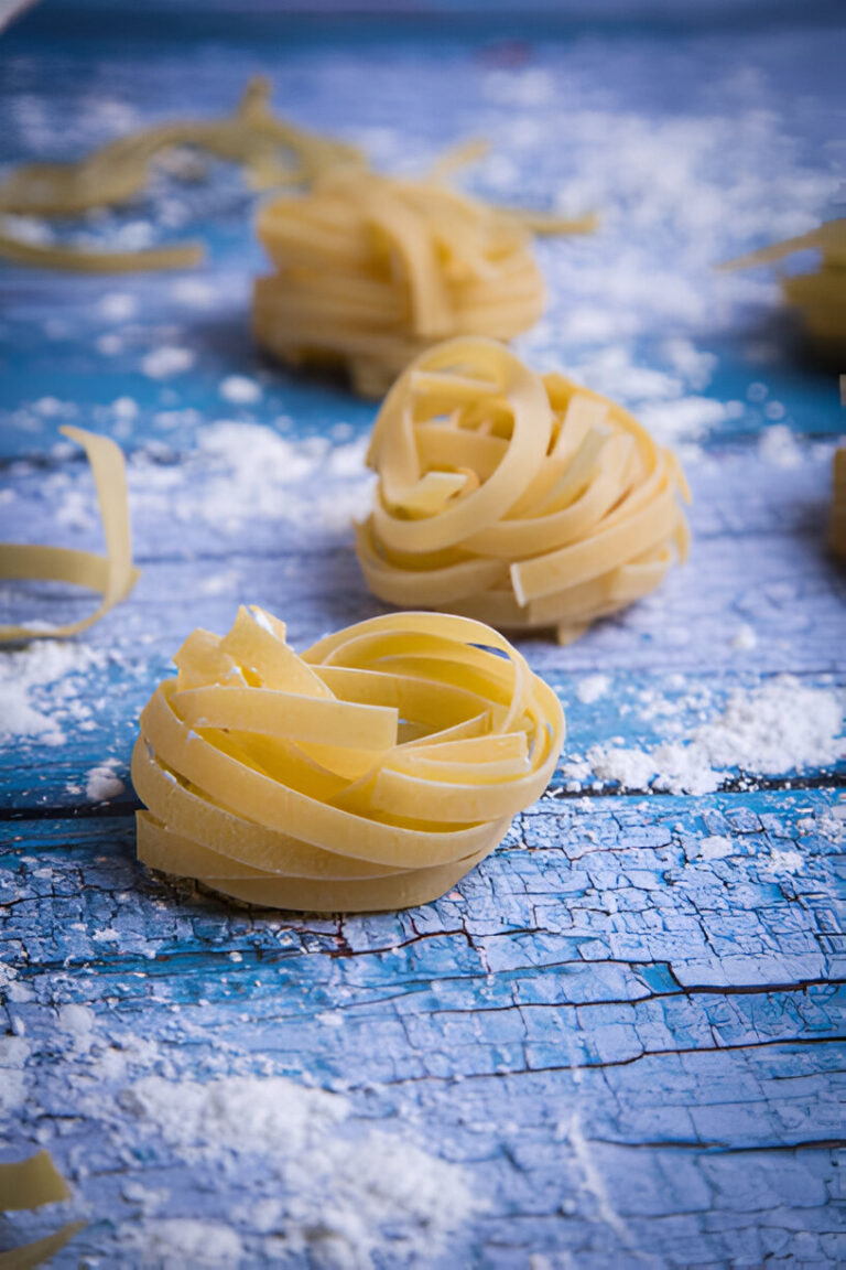 Freshly made pasta nests on a textured blue wooden surface dusted with flour