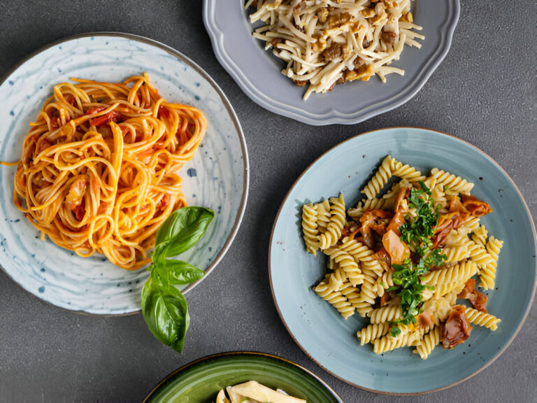 A colorful display of different pasta dishes on plates, including spaghetti, fusilli, and a side of noodles, garnished with basil.