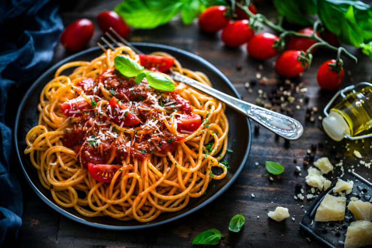 A plate of spaghetti topped with tomato sauce, fresh basil, and grated cheese, with cherry tomatoes and olive oil in the background.