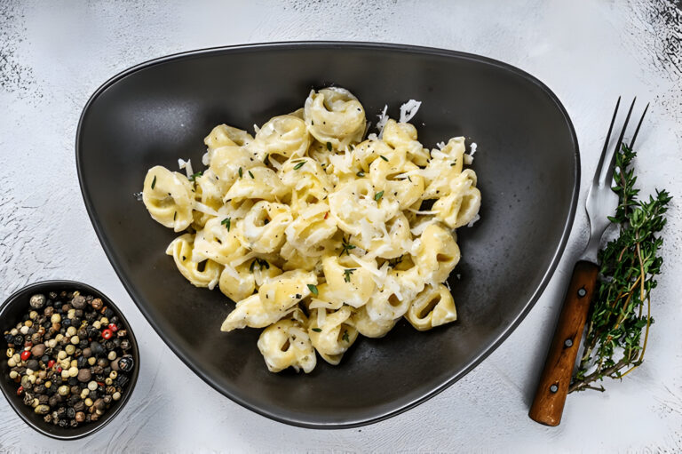 A bowl of creamy pasta with herbs and a side of mixed peppercorns and a fork.