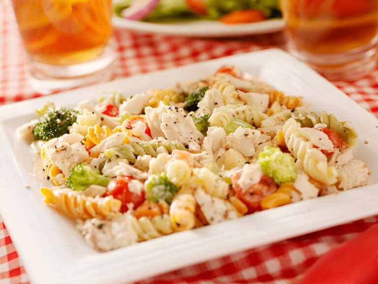 Colorful pasta salad with vegetables on a white plate, served on a red checkered tablecloth.