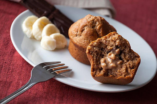 A freshly baked muffin cut in half, revealing a filled center, accompanied by banana slices and a fork on a white plate.