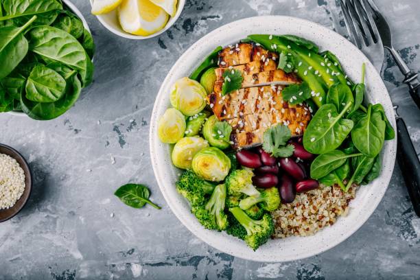 A healthy bowl of grilled chicken, quinoa, and assorted vegetables including broccoli, Brussels sprouts, and spinach, garnished with sesame seeds and cilantro.